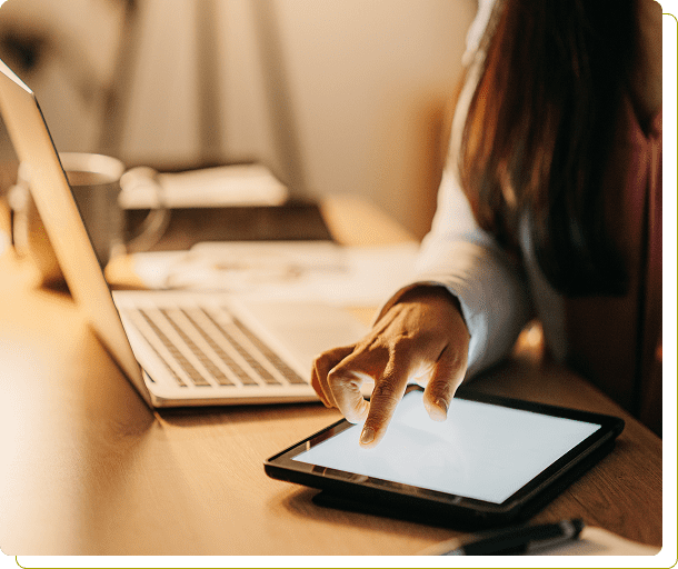 Person using tablet near open laptop.